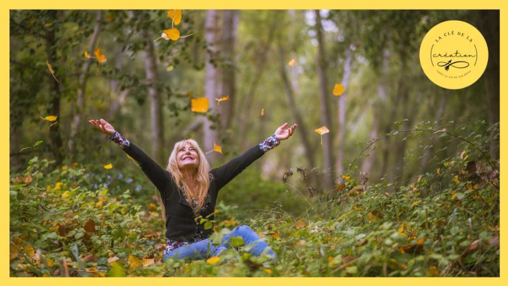 Femme resplendissant de bonheur assise dans une clairière avec des feuilles qui tombent