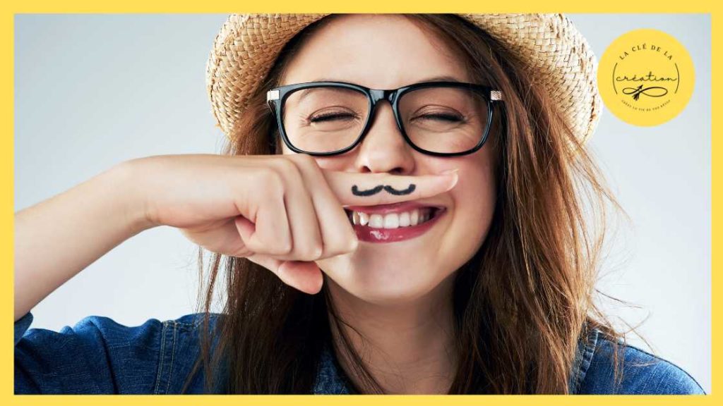Jeune femme avec un chapeau de paille et des lunette qui rigole parce qu'elle a dessiné une moustache sur son doigt qu'elle a mis sous son nez.